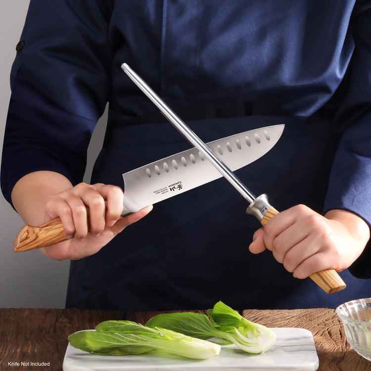 Person holding a knife with olivewood handle and a honing steel with wooden handle, sharpening the blade.