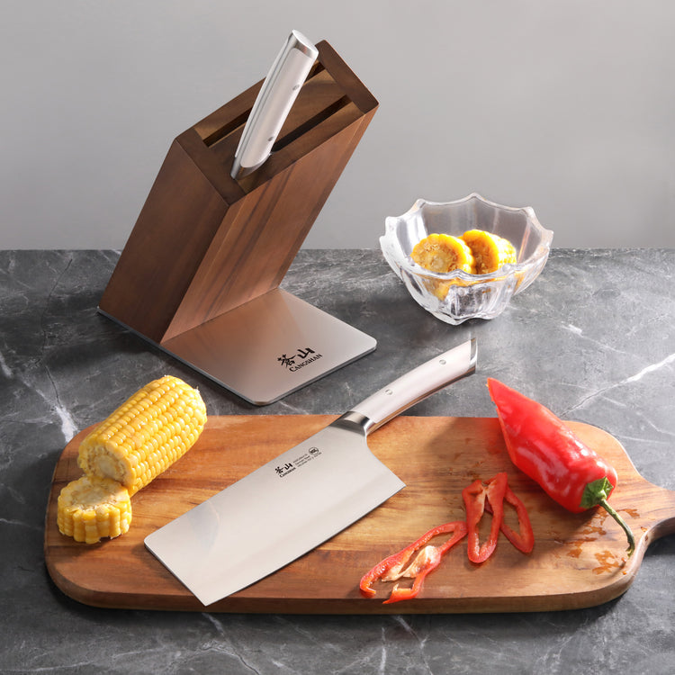 Cleaver knife block set with one knife in block, one cleaver on wooden board with sliced corn and red pepper, and glass bowl