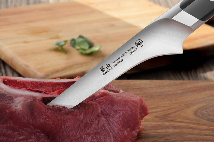 Knife blade cutting into raw red meat on a wooden surface with a cutting board and basil leaves in the background.