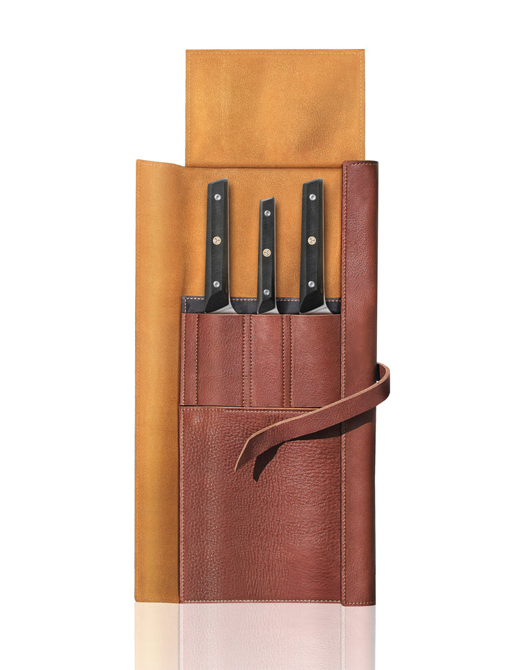 Four knives with black handles in a brown leather roll with pockets and a tie closure, roll partially open.