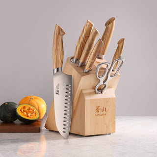 
                    
                      Knife block set with six knives and kitchen scissors, wooden handles and block, on marble surface with cut pumpkins nearby.
                    
                  