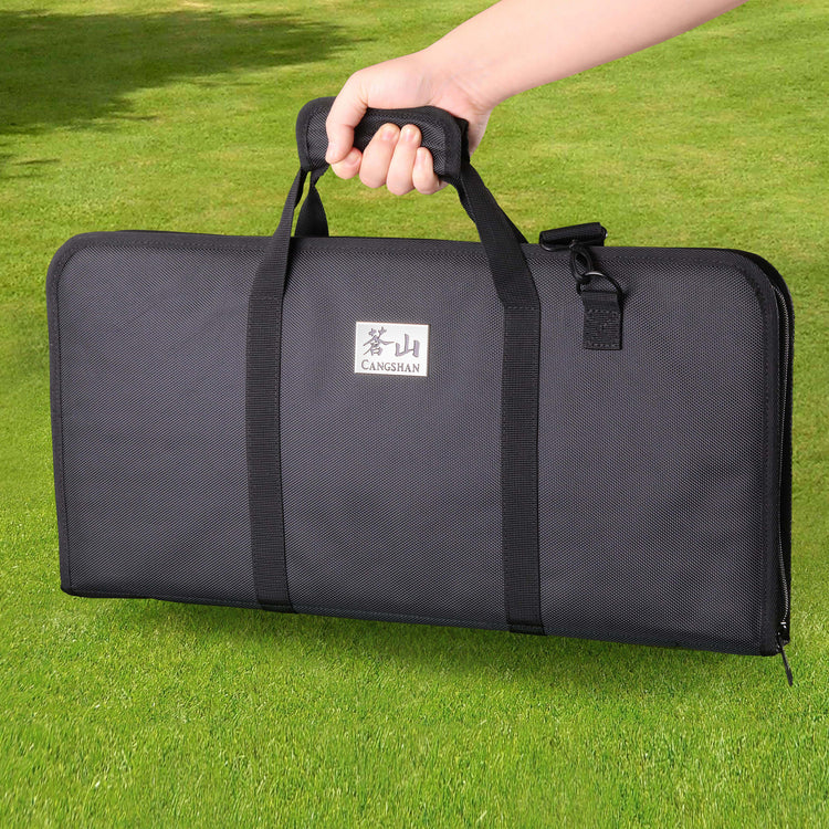 Black rectangular carrying bag with handles held by a hand, placed on green grass.