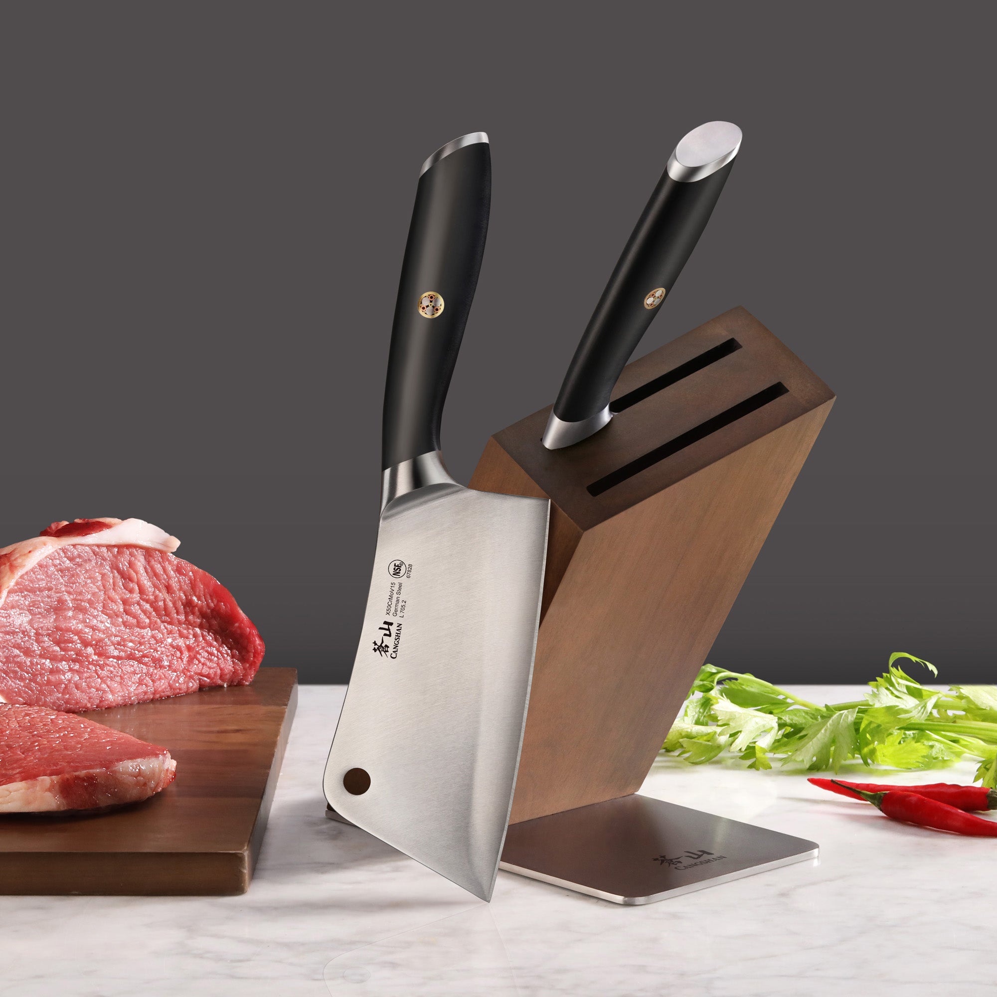 Two black-handled cleaver knives in a wooden block next to raw meat and herbs on a marble surface.
