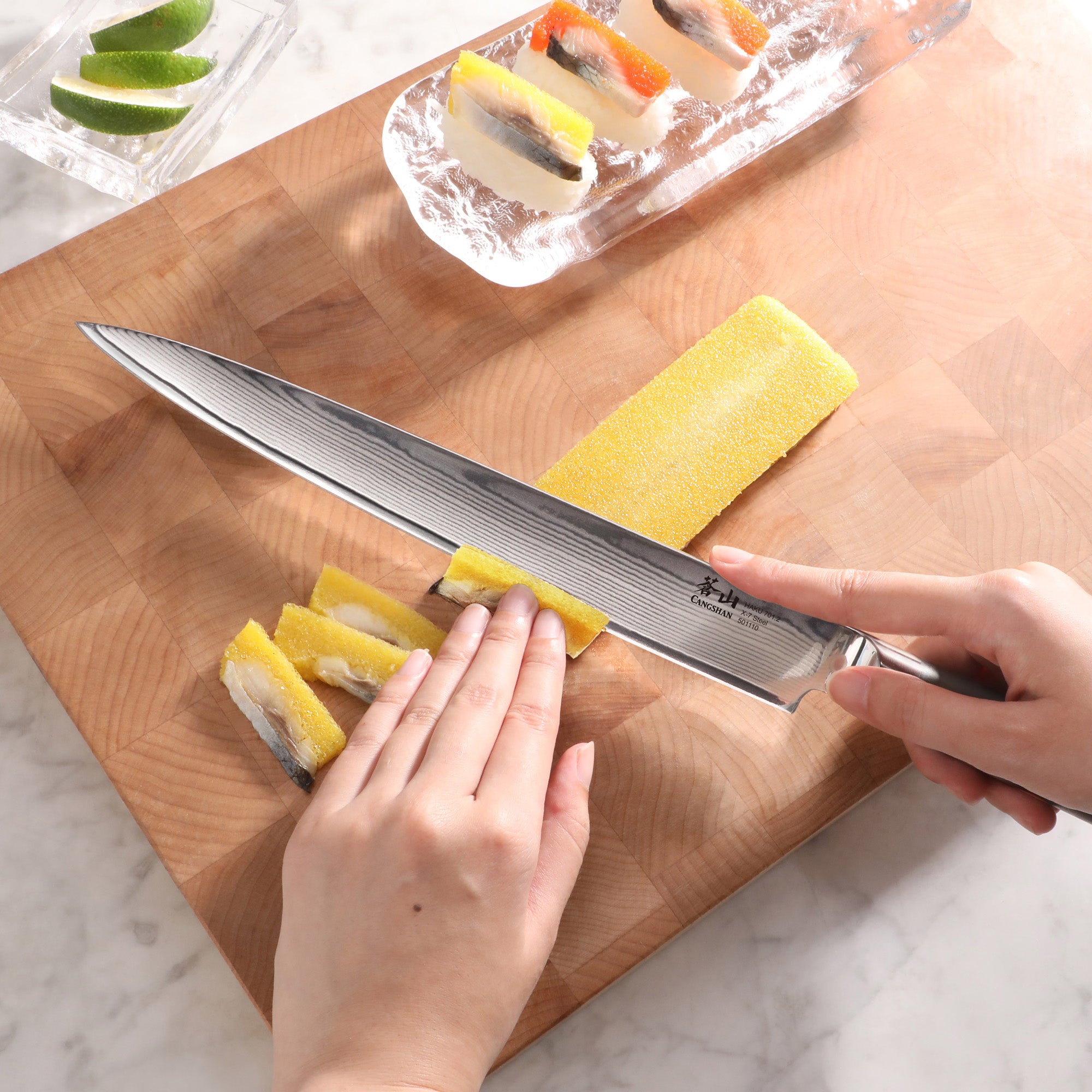 Person slicing yellow fruit with a 10-inch Damascus steel sashimi knife on a wooden cutting board.