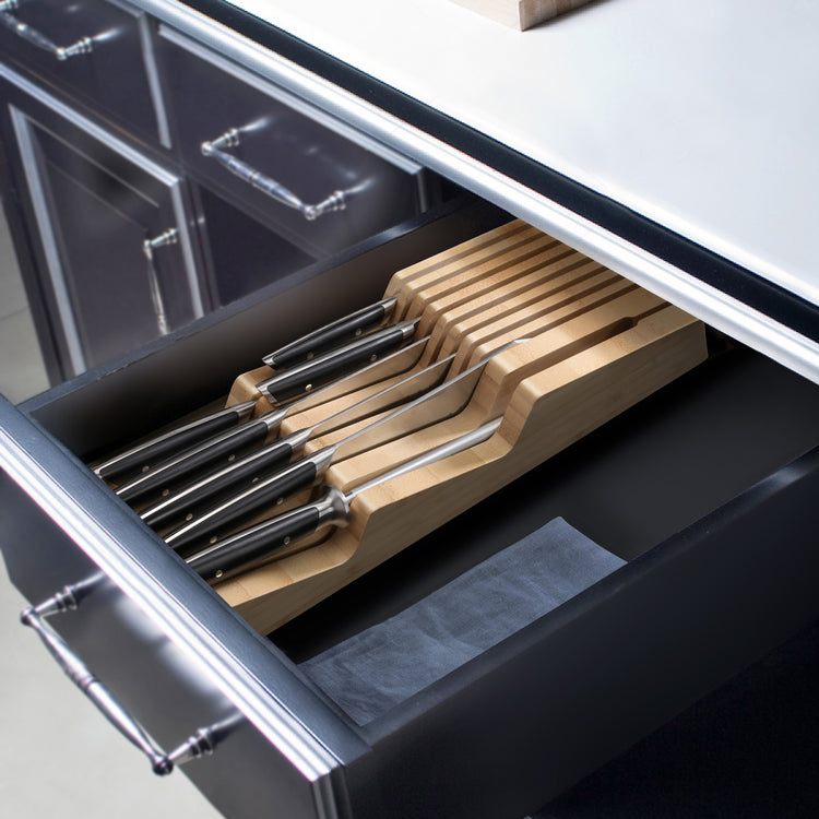 Set of eight BBQ knives with black handles neatly arranged in a bamboo in-drawer knife block inside a kitchen drawer.