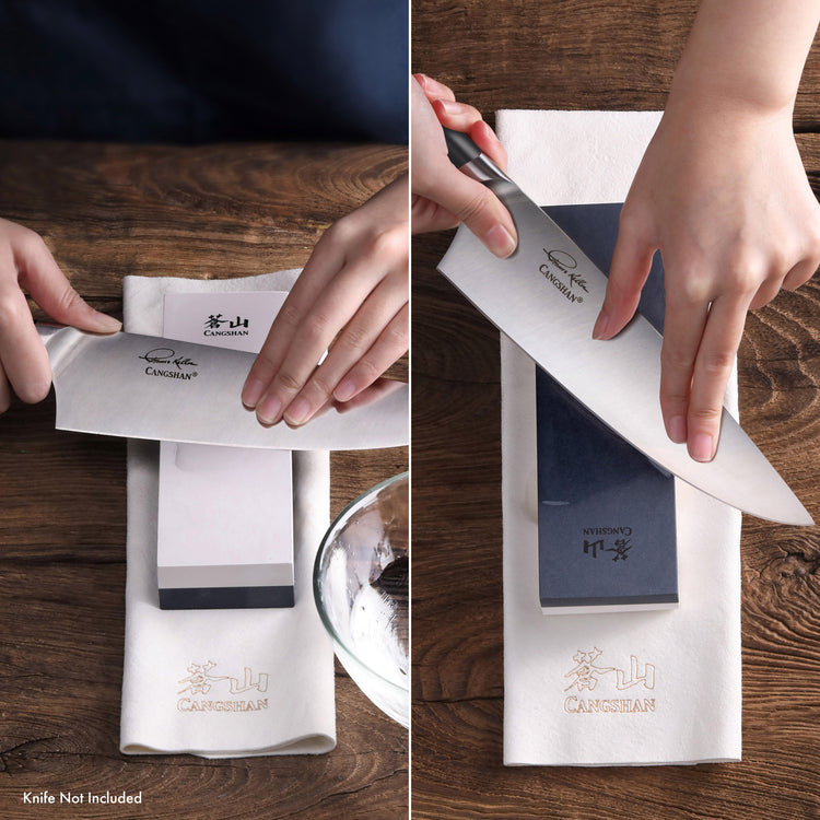 Hands sharpening a kitchen knife on a whetstone placed on a white cloth with a wooden surface background.