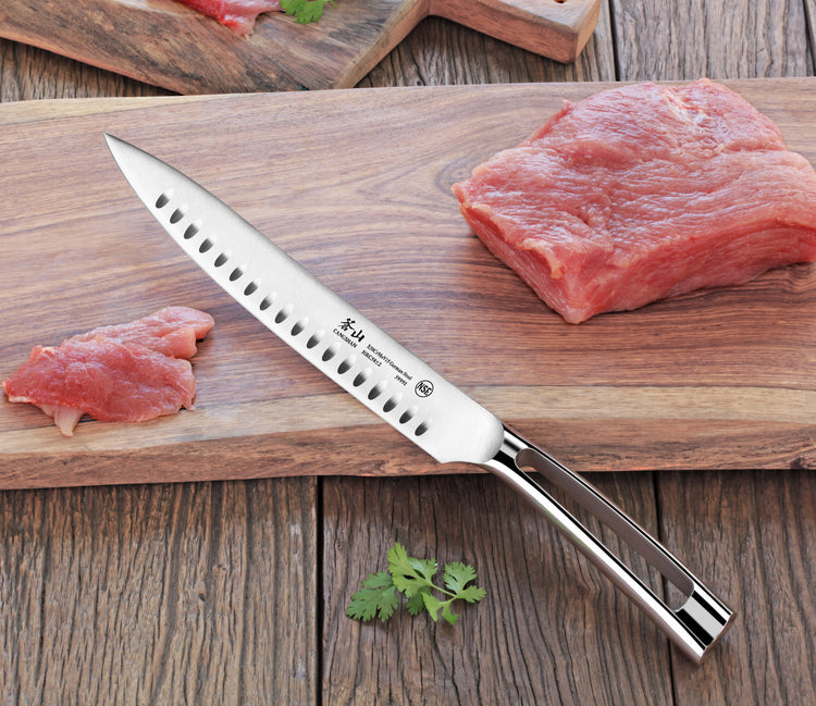 9-inch carving knife with hollow edge and metal handle on wooden cutting board with raw meat pieces.