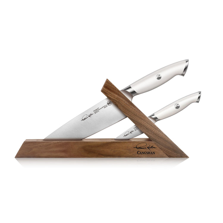 Two knives with white handles in a walnut triangular block, signed by Thomas Keller, on a white background.