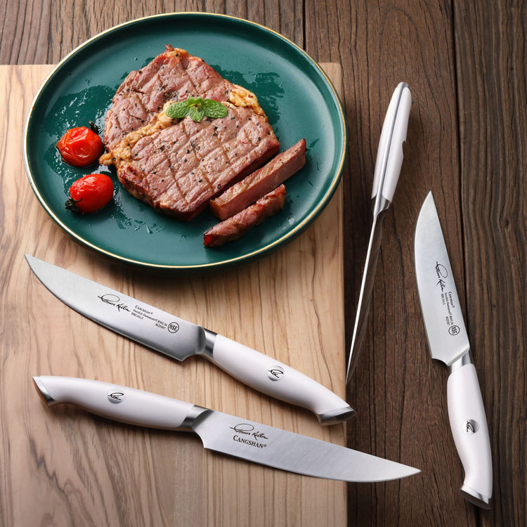 Grilled steak with roasted tomatoes on a green plate, alongside three white-handled steak knives and a meat fork on a wooden