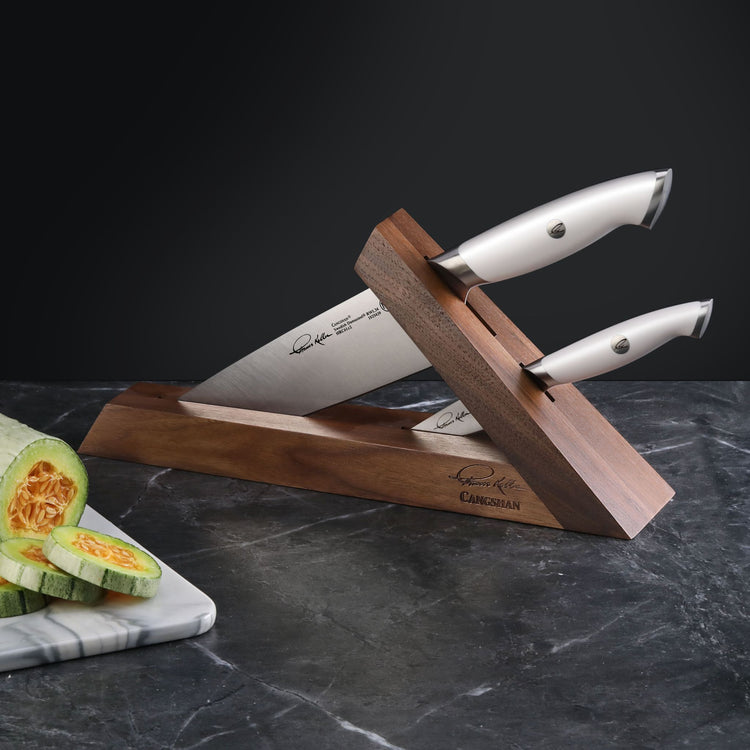 Wooden knife block holding two knives with white handles on a dark countertop next to sliced squash.