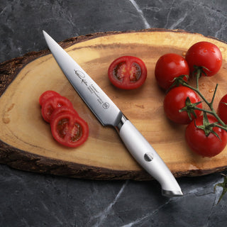 
                    
                      White-handled utility knife with stainless steel blade slicing red tomatoes on a wooden cutting board.
                    
                  