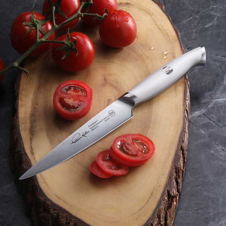 Utility knife with stainless steel blade and handle on wooden cutting board with sliced and whole tomatoes.