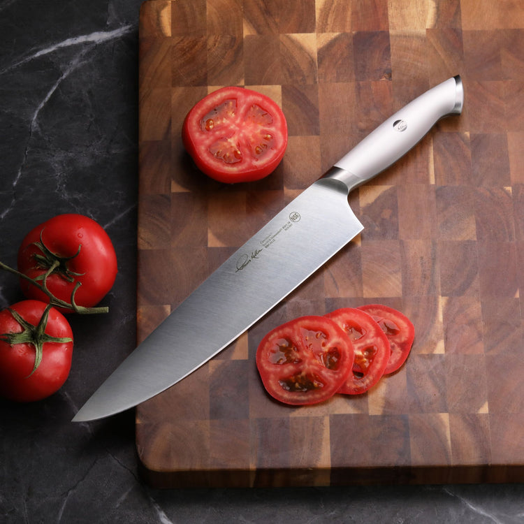 10-inch chef's knife with white handle on wooden cutting board, sliced and whole tomatoes nearby.